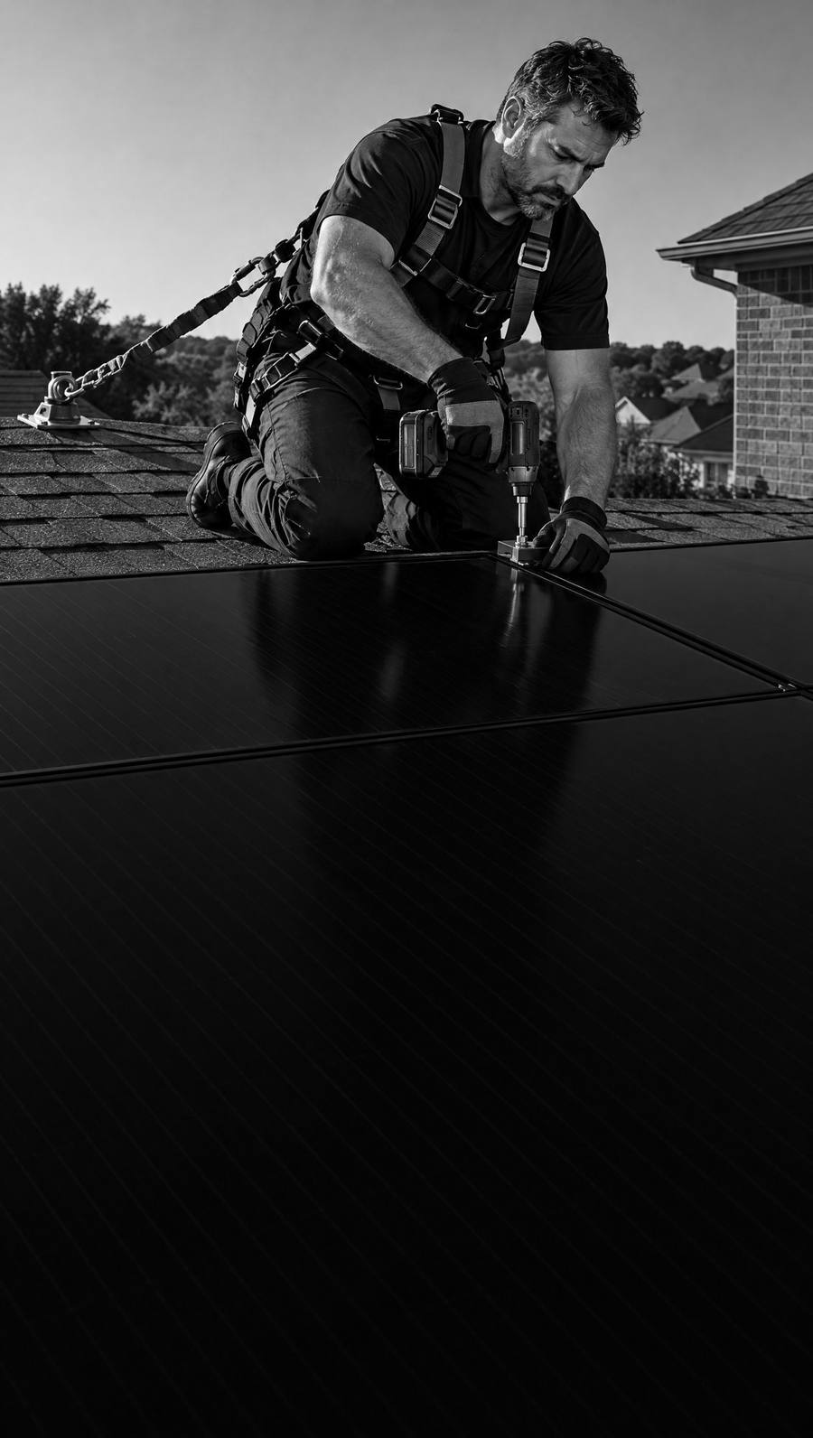 A crew lead in a fall-protection harness fastens a solar panel on a roof.